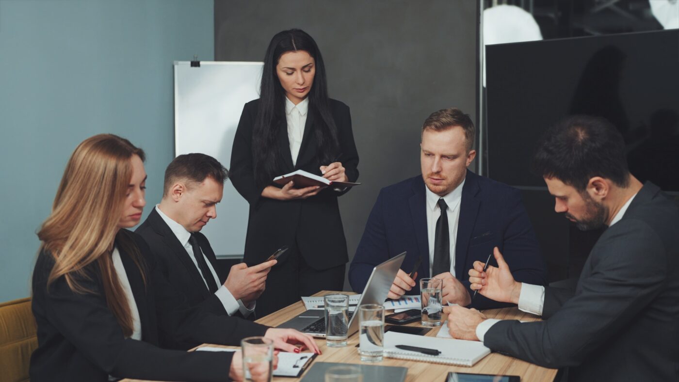 Leadership team in a boardroom actively discussing strategy around a table with laptops and notes, representing collaborative decision-making and strategic execution.